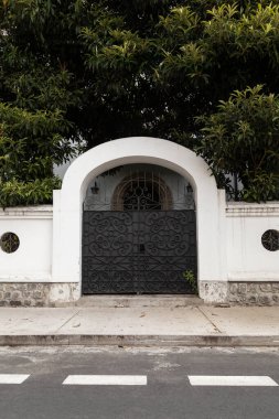 Ağaçların çerçevelediği bir çiftliğe açılan siyah kemerli bir kapı. Kapının zarif tasarımı ve çevreleyen yeşillik bir karşılama yaratıyor.