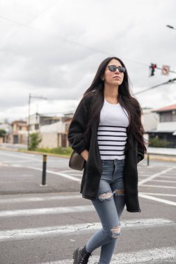 Kot pantolon giymiş güzel bir kadın ve siyah bir trençkot giymişti. Sokakta rahatça dolaşıyordu. Rahat temposu ve zahmetsiz stili onu ayakta tutuyor.