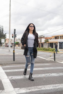 Trençkotunun cebinde elleri olan güzel bir kız şehirde yürüyor. Kendine güveni ve gevşemiş tavrı şehre cazibe katıyor.