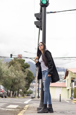 Yol kenarından alınmayı bekleyen güzel bir kadın, bir trafik lambasının yanında. Sakin tavrı ve şehirli hali.