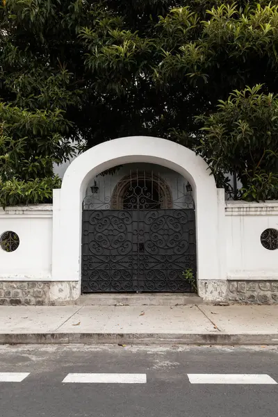 Ağaçların çerçevelediği bir çiftliğe açılan siyah kemerli bir kapı. Kapının zarif tasarımı ve çevreleyen yeşillik bir karşılama yaratıyor.