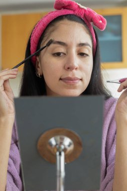 A beautiful girl carefully shaping and filling her eyebrows with makeup. Perfect for beauty, makeup artistry, and self-care content. clipart