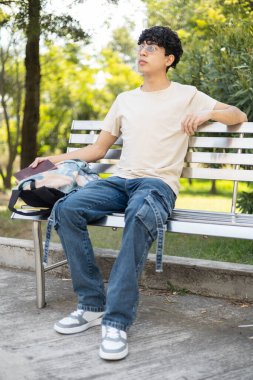 Parktaki bankta dinlenen genç bir insan, güneşli güzel bir günün tadını çıkarıyor, rahatlama, açık hava eğlencesi ve huzurlu anlar gibi konular için mükemmel..