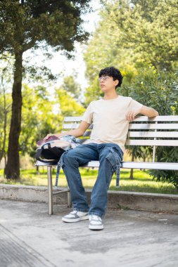 Parktaki metal bir bankta oturan genç bir çocuk, dışarıda eğleniyor. Rahatlama, açık hava aktiviteleri ve park hayatı temaları için ideal.