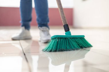  Yerleri süpüren, bacaklarını ve ayakkabılarını gösteren, kot giyen, temizlik, ev işleri ve ev işleri için mükemmel bir kadın..