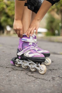 Mor bir pateni ayarlayan elleri gösteren yakın plan bir çekim, sadece kızların bacaklarının alt kısmı görünür, paten ve hareketlere odaklanmış..