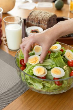 Taze bir salatadan kaynamış bir yumurtayı dikkatlice seçerken yakından çekilen bir el, domates, marul ve zeytinyağlı çiseleme ile, gündelik bir zevk anı yaratıyor..