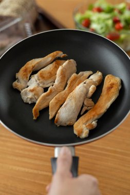 Altın renginde, kızarmış tavuk şeritleri tavada cızırdıyor, kokuları havayı doldururken, arka planda canlı bir domates salatası ürkütücü bir şekilde duruyor..