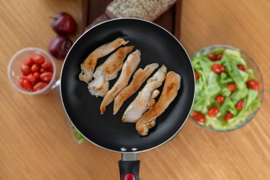 Altın renginde, kızarmış tavuk şeritleri tavada cızırdıyor, kokuları havayı doldururken, arka planda canlı bir domates salatası ürkütücü bir şekilde duruyor..