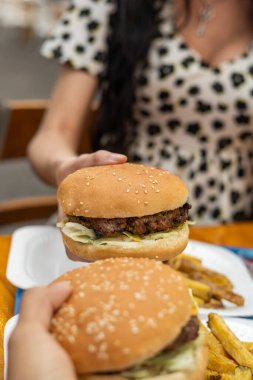 İki insan hamburger ve patates kızartmasından hoşlanır. Elleri lezzet ve bağlantı dolu sıradan, paylaşılan bir anda yiyeceğe uzanır..