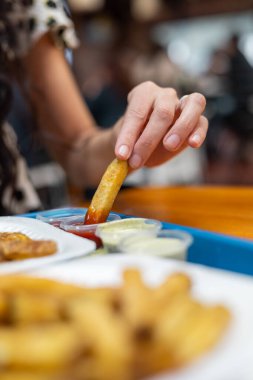 Bir kol, ketçapa batırılmış, gevrek bir patates kızartmasına uzanır ve tesadüfi bir yemek deneyiminde hoşgörünün özünü yakalar..