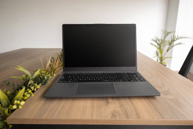 Şık bir dizüstü bilgisayar, modern ofis ortamında teknoloji ve kırsal çalışma alanlarını harmanlayan doğal bir ahşap çalışma masasının üzerinde yer alır..