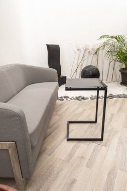 Laptop kullanımı için tasarlanmış kompakt metal bir masanın yanında şık gri bir kanepe üretken çalışma oturumları için mükemmel bir konfor ve fonksiyon karışımı oluşturuyor..