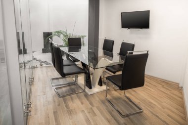 Pürüzsüz siyah sandalyelerle çevrili şeffaf cam bir masanın yer aldığı modern bir toplantı odası, tartışma ve işbirliği için şık ve profesyonel bir ortam yaratıyor..