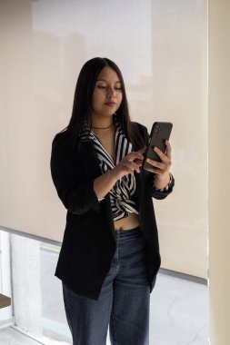 Genç bir kadın kameraya bakar, tabletini dikkatle incelerken beyaz tahtanın yanında durur. Bu görüntü modern ofis ortamında odak, teknoloji kullanımı ve profesyonelliği aktarır..