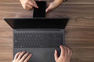 Dinamik yukarıdan çekim, bilgisayarı ve akıllı telefonu ustalıkla yöneten, modern çoklu görev ve kusursuz dijital bağlantıyı yansıtan eller yakalıyor..