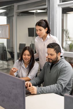 İş arkadaşları en son satış raporlarını incelerken ekrana odaklanıyorlar, modern, açık ofis ortamında işbirliği yapıyorlar..