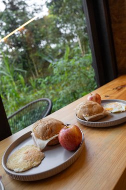Taze yiyecek tabakları, tost, meyve ve kahve olan bir kahvaltı barı. Sıcak doğal ışık, sabah yemekleri için mükemmel, davetkar bir ortam yaratır..