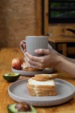 Sıcak bir kahve bardağını nazikçe pencerenin önünde tutarken, doğal ışık içeri doluyor, huzurlu ve rahat bir sabah atmosferi yaratıyor.