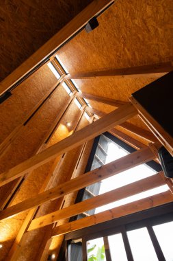 Bir glamping kabin, doğal elementlerle geometrik stili harmanlayan, tahtadan yapılmış çarpıcı üçgen bir çatı içerir. Eşsiz tasarımı orman çevresinde göze çarpar..