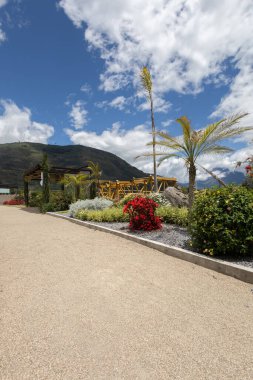 Zengin bitkiler, renkli çiçekler ve yeşil yapraklarla dolu halka açık bir meydanın çarpıcı girişi rahatlatıcı ve açık hava keyfi için ideal doğal bir ortam yaratıyor..