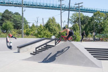 Patenciler ve motorcular numaralarını güneşli bir yaz gününde halka açık olan açık bir kaykay parkında yapıyorlar.