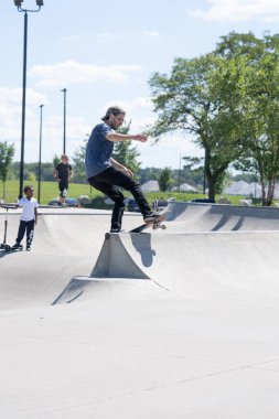 Patenciler ve motorcular numaralarını güneşli bir yaz gününde halka açık olan açık bir kaykay parkında yapıyorlar.