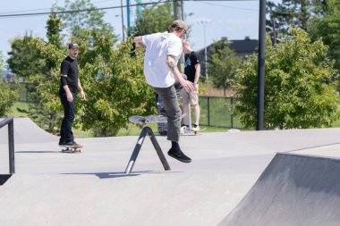 Patenciler ve motorcular numaralarını güneşli bir yaz gününde halka açık olan açık bir kaykay parkında yapıyorlar.