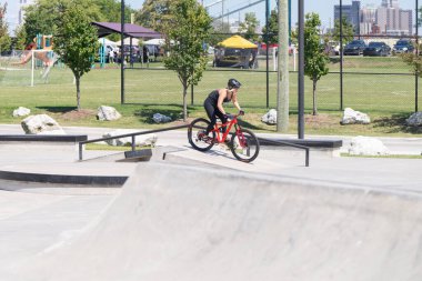 Patenciler ve motorcular numaralarını güneşli bir yaz gününde halka açık olan açık bir kaykay parkında yapıyorlar.