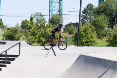 Patenciler ve motorcular numaralarını güneşli bir yaz gününde halka açık olan açık bir kaykay parkında yapıyorlar.