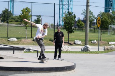 Patenciler ve motorcular numaralarını güneşli bir yaz gününde halka açık olan açık bir kaykay parkında yapıyorlar.