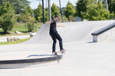 Patenciler ve motorcular numaralarını güneşli bir yaz gününde halka açık olan açık bir kaykay parkında yapıyorlar.