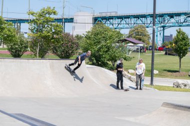Patenciler ve motorcular numaralarını güneşli bir yaz gününde halka açık olan açık bir kaykay parkında yapıyorlar.
