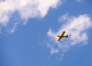Sarı itfaiye uçağı mavi gökyüzünün altında uçuyor.
