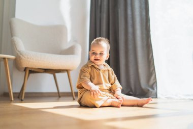 Genç bir erkek çocuk önünde bir sandalyeye bakarak yerde oturmaktadır. Duruşu rahat, elleri dizlerinin üzerinde dinleniyor. Sandalye sağlam ve davetkar görünüyor. Düzgün bir pozisyonda..