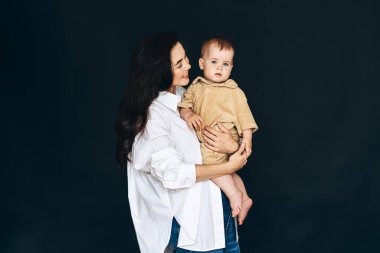 Bir kadın, kucağında bir bebekle ayakta duruyor. Kadın yüzü, bebekle ilgilenirken şefkatini göstermektedir. Bebek, kadınların içinde mutlu ve güvende görünüyor..