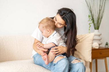 Bir kadın kanepeye oturmuş, kucağında bir bebek besliyordu. Kadının bebekle ilgilenirken ifadesi odaklanmış ve sevecendir. İkisi de bağlarında rahat ve memnun görünüyorlar..