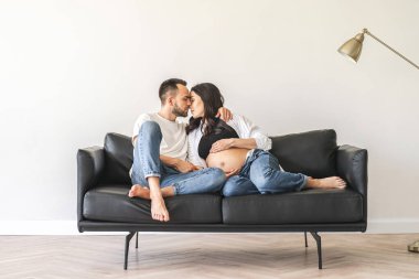 Bir erkek ve bir kadın kanepede otururken şefkatle kucaklaşıyorlar, yakınlık anlarını paylaşıyorlar.