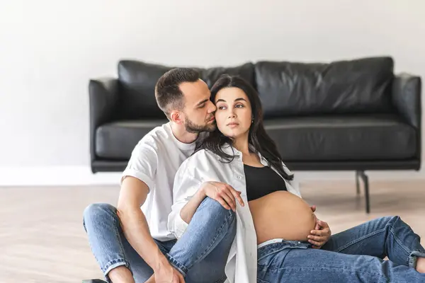 一对怀孕的夫妇坐在客厅的地板上 一边谈着话 一边在家里布置家具 免版税图库图片