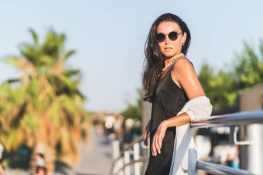 Güneş gözlüğü takan bir kadın manzaraya tepeden bakan bir tırabzana yaslanır..