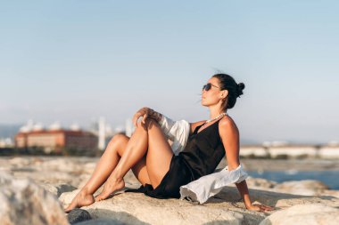 Bir kadın su kütlesinin yanındaki kayaya tünemiş..