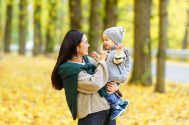 Bir kadın, düşen yapraklarla dolu bir parkta dururken küçük çocuğunu kollarına alır. Gülümsüyorlar ve birbirlerine bakıyorlar..