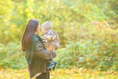 Sonbahar ormanında ayakta duran bir kadın bebeğini kollarında tutar..