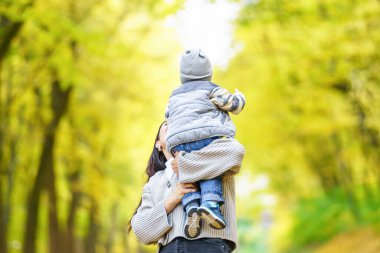 Bir anne, altın yapraklarla dolu bir ormanda yürürken oğlunu kollarına alır..