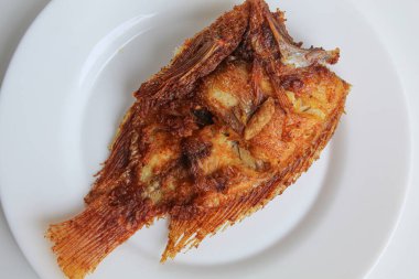 Beyaz bir tabakta kızarmış kırmızı tilapia balığı, beyaz arka planda izole edilmiş.