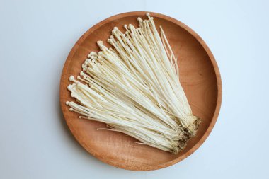 Enoki mushroom, or enokitake or Flammulina filiformis, on wooden plate, isolated on white background clipart