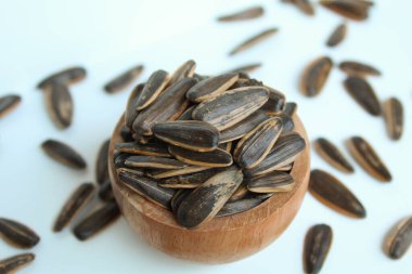 Pile of sunflower seed on a wooden bowl. Sunflower seed with striped shell. Isolated on white background clipart