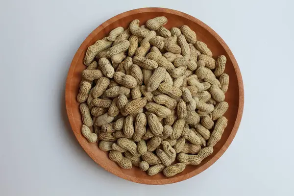 Yer fıstığı, yer fıstığı ya da maymun fındığı, ya da Arachis hipogaea, beyaz arka planda izole edilmiş, tahta bir tabakta. Atıştırmalık olarak hazır.