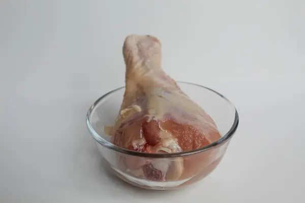 Şeffaf bir kasede çiğ tavuk budu. Beyaz arkaplanda izole.