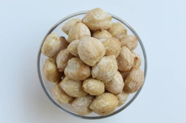 Kurumuş Endonezya Candlenuts, ya da Kemiri, Aleurite Moluccanus 'un tohumu, şeffaf bir kasenin içinde, beyaz arka planda izole edilmiş. Düz ya da üst görünüm